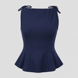 Sleeveless peplum top with boat neckline, shoulder tie accents, sculpted seams, and tailored waist for an elegant structured silhouette